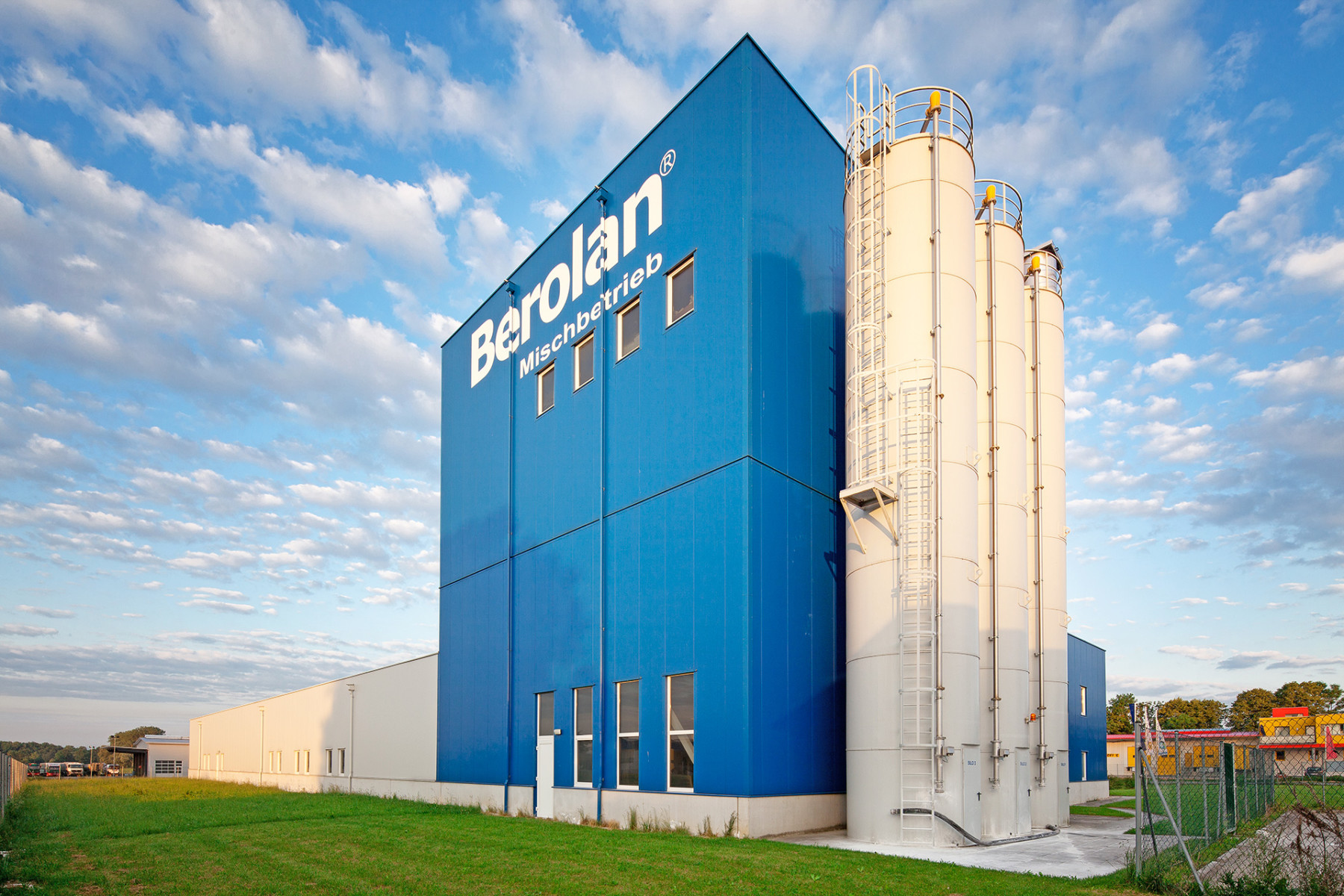 Blaues, hohes Firmengebäude der BEROLAN GmbH mit drei großen Hochsilos